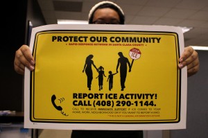 A rapid responder trainee holds a yellow poster with the words "PROTECT OUR COMMUNITY, REPORT ICE ACTIVITY! CALL (408) 290-1144" and an image of a family walking.