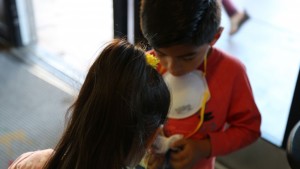 A girl and a boy wearing a smoke mask stand in front of a window.