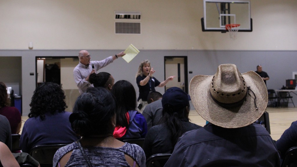 A crowd watches a man and a sign language interpreter in a high school gymnasium.