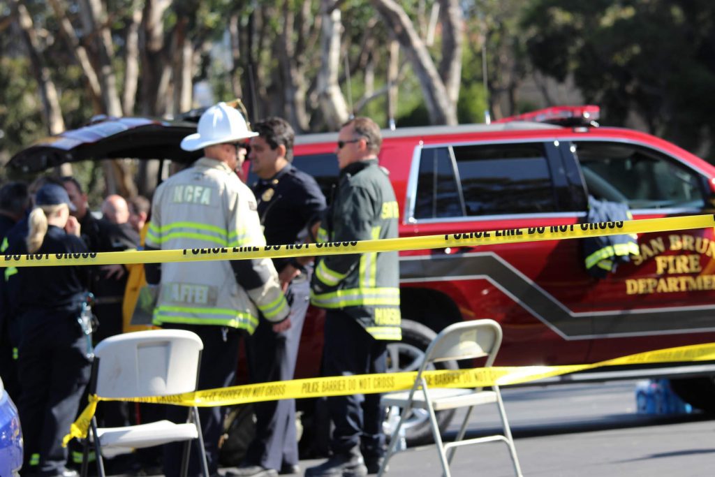 Inside a police perimeter, fire officials gather near a car that says "San Bruno Fire Department."