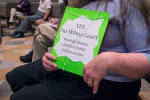 Jen Stokely, Executive Director of “Housing Choices”, holding up a sign reading “YES for Wilton Court”. 