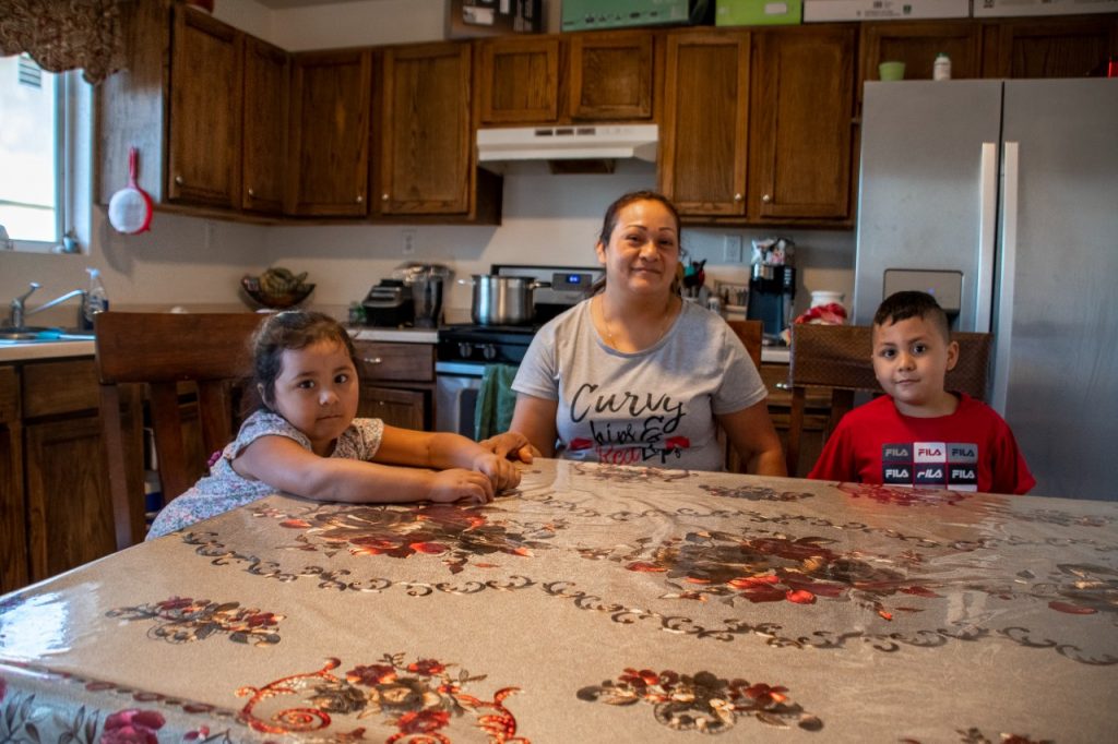 A mother and her two small children sit in their kitchen.