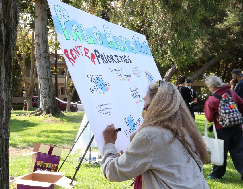 A woman is squatting down and writing on a poster board