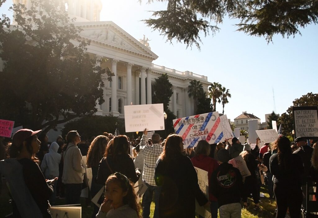 A crowd stands in front of the California Capitol holding up signs.