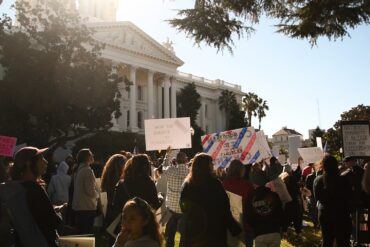 A crowd stands in front of the California Capitol holding up signs.