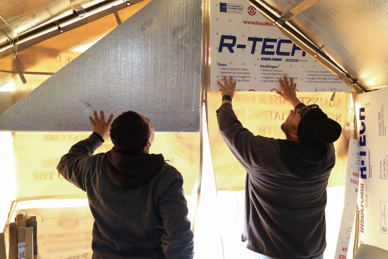 Two men install insulation.