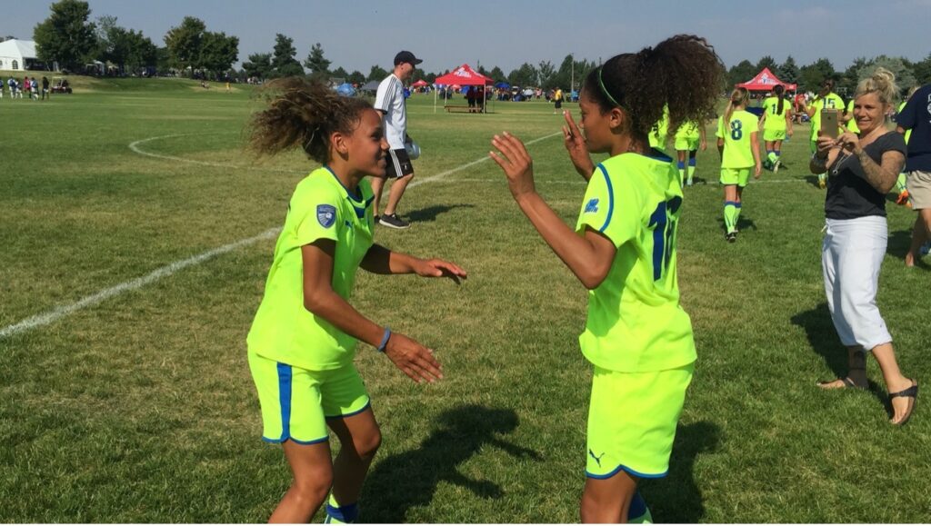 Two girls facing each other in bright green soccer uniforms