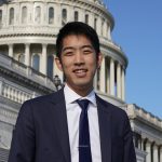Foto de la cabeza de Evan Bing, un sonriente hombre asiático de 22 años con traje y corbata frente al Capitolio de EE. UU.