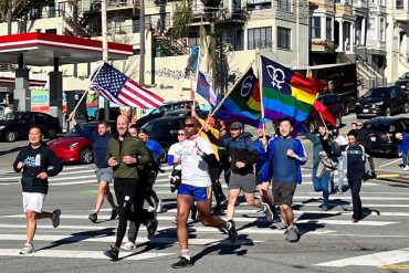 A group of people running on the street carrying an American flag and a rainbow flag.