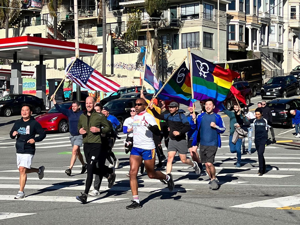 A group of people running on the street carrying an American flag and a rainbow flag.