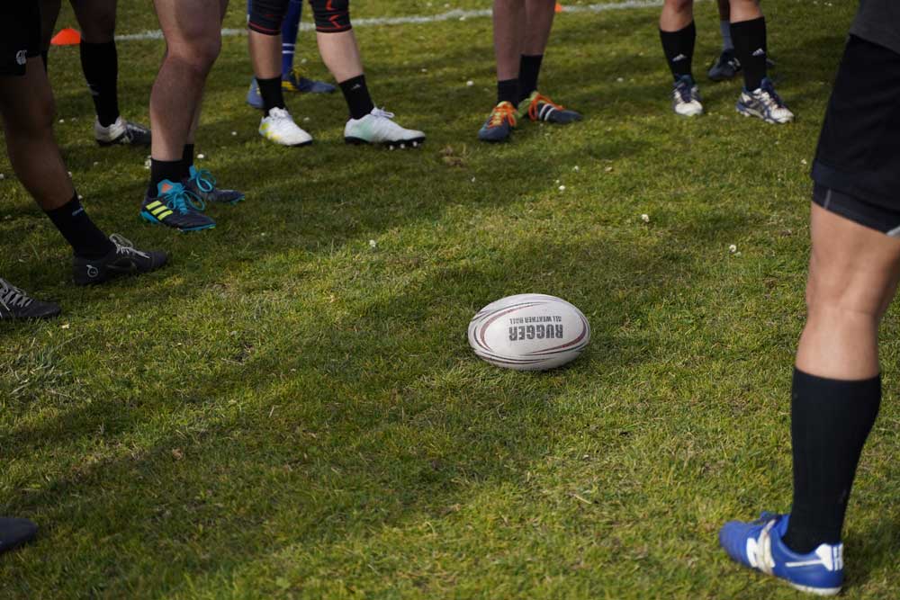 A rugby ball is on the field, surrounded by the feet of rugby players.