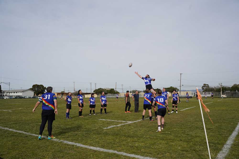 A wide shot of rugby players. One is leaping in the air.