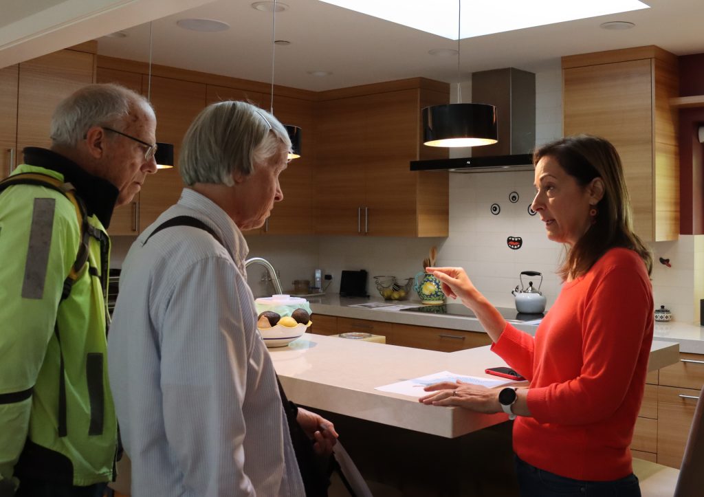Three people talk by a kitchen island, an induction stove is in the background.
