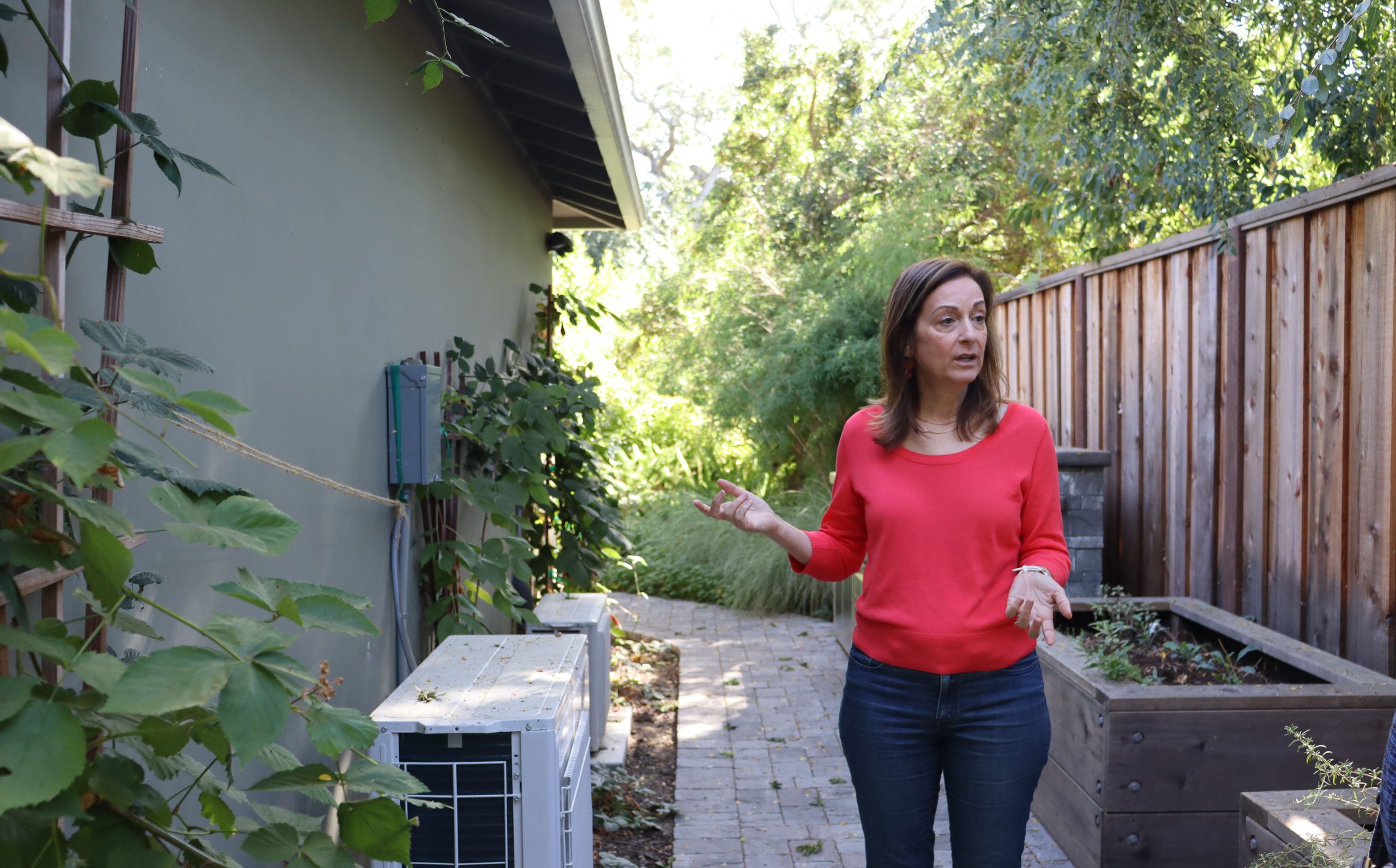 A woman in a red shirt stands next to a house.