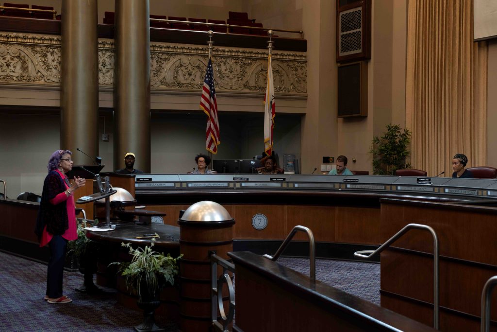 A woman standing behind a podium talking to a panel of people.