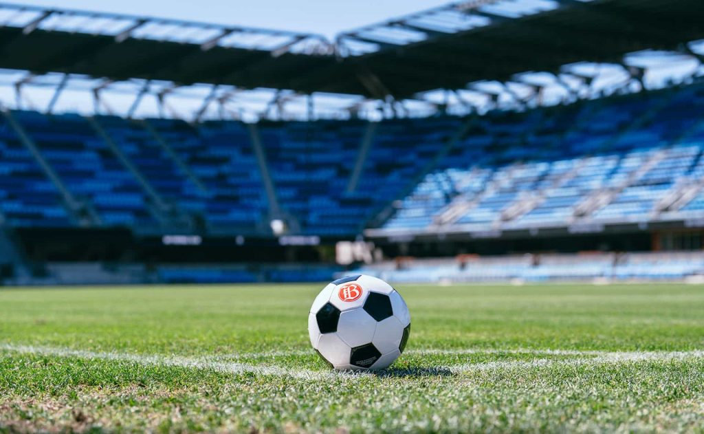 A soccer ball is on a field of a stadium. Seats are in the background.