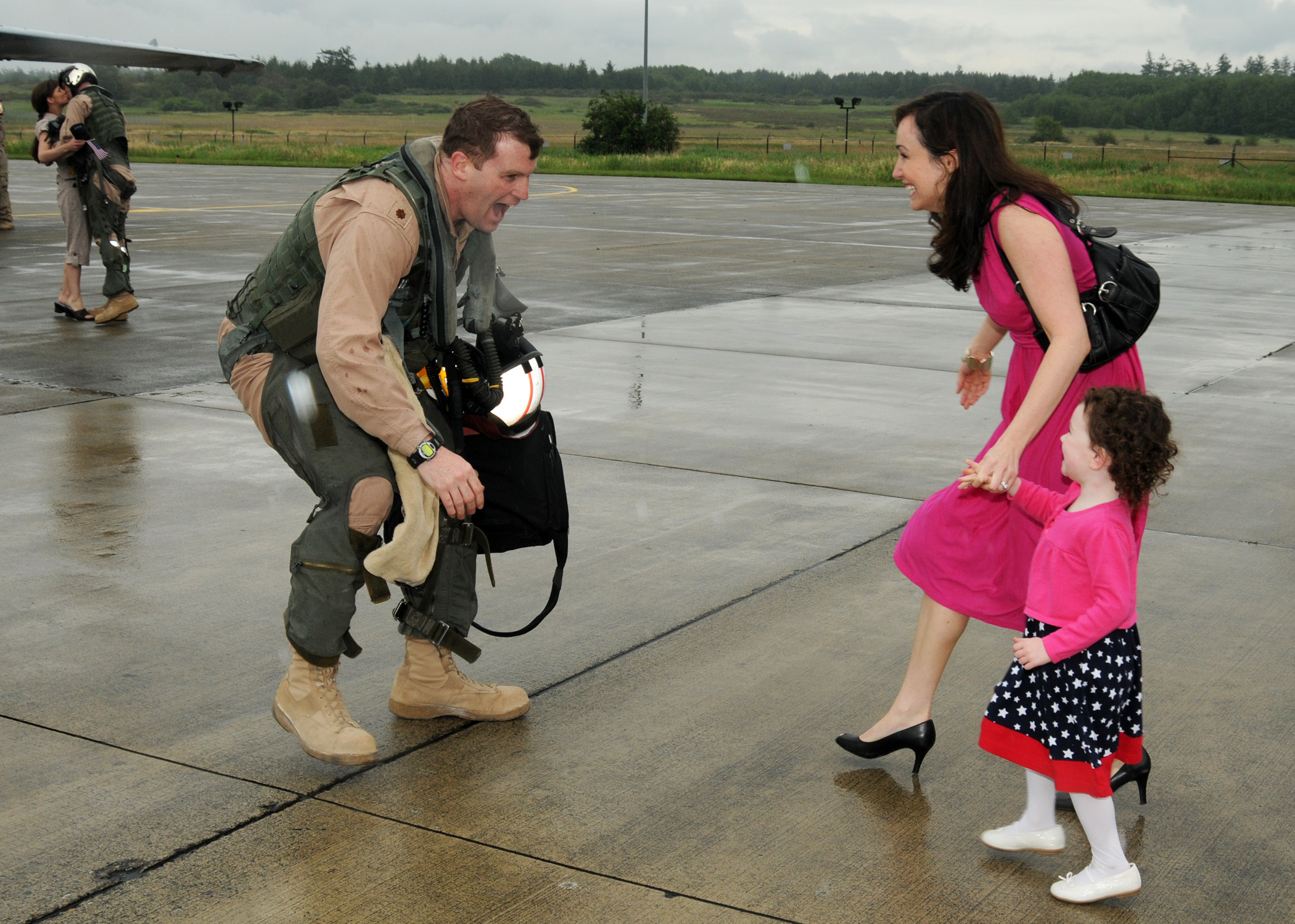 A man stoops in military uniform stoops down as a woman and a child runs toward him.