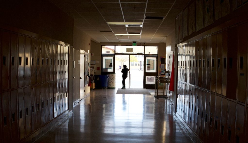 A picture of a school hallway and a person's outline seen through a doorway.