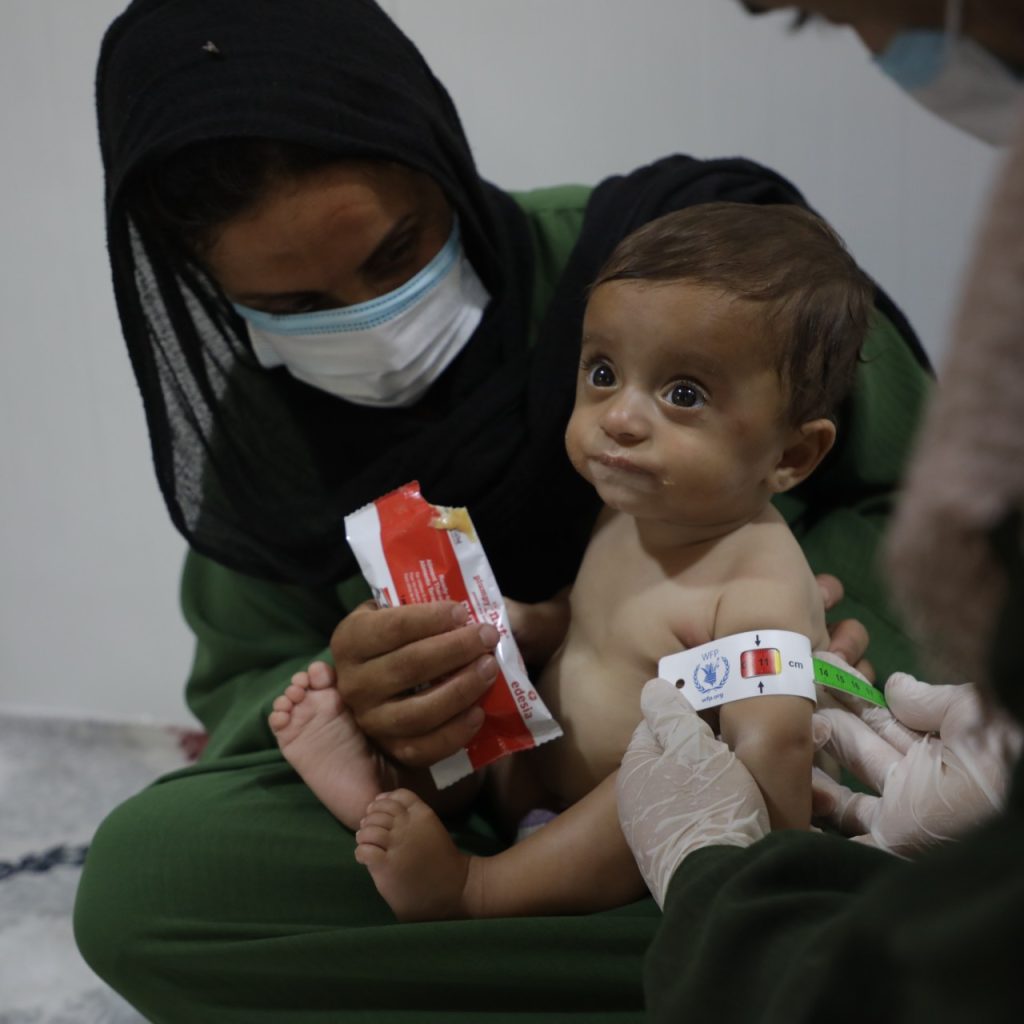 Safaa, being screened for acute malnutrition at Save the Children's nutrition center in Northeast Syria editedJPG A child is sitting on an adult's lap.