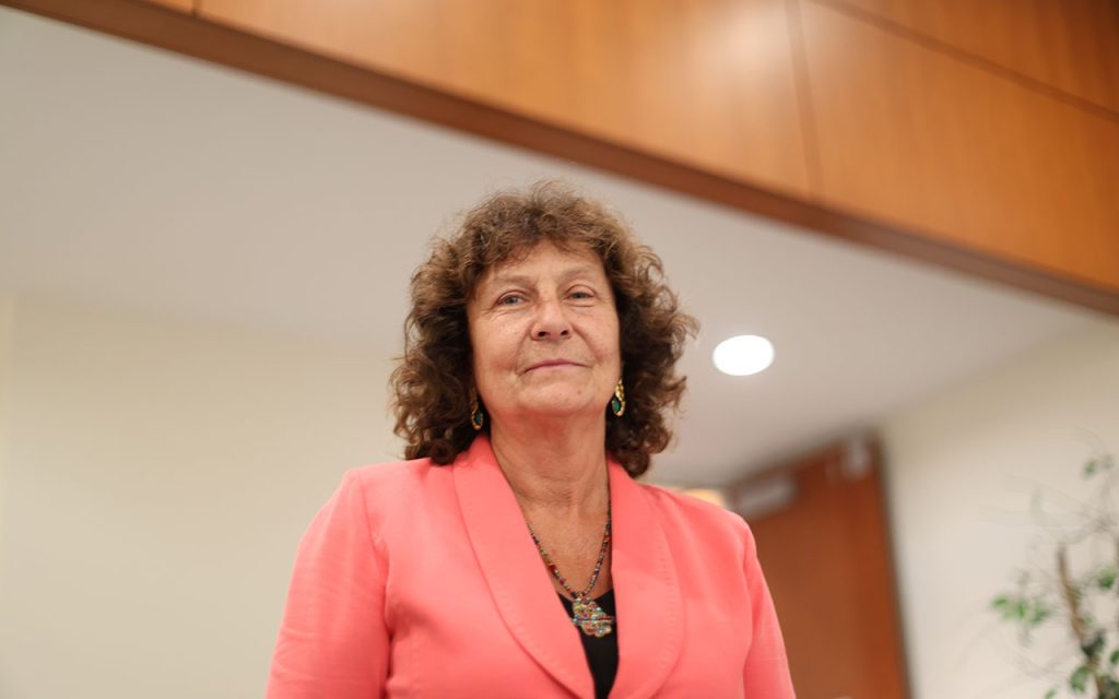 A woman in a pink blazer looks at the camera.