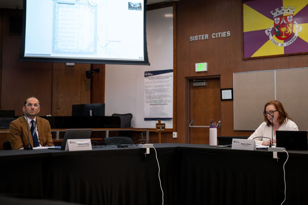 Two people on a panel sits and looks at a presentation.