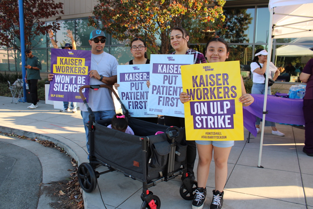 Striking worker stands with his  family holding up signs.