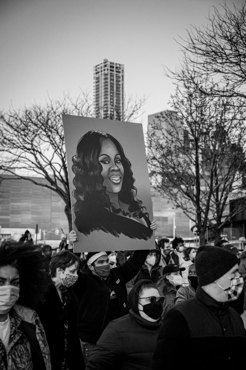 Someone in the crowd holds up a painting of Breonna Taylor.