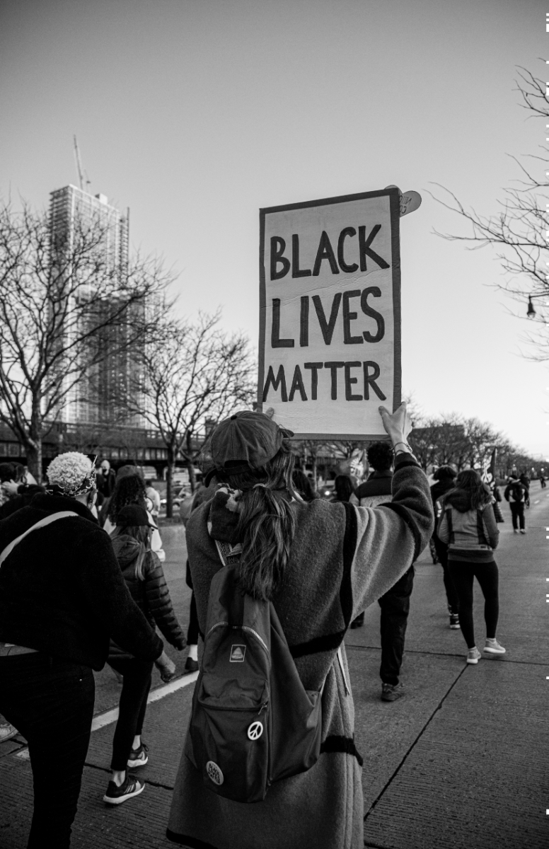 A protester photographed from behind is holding up a 'Black Lives Matter' sign. 