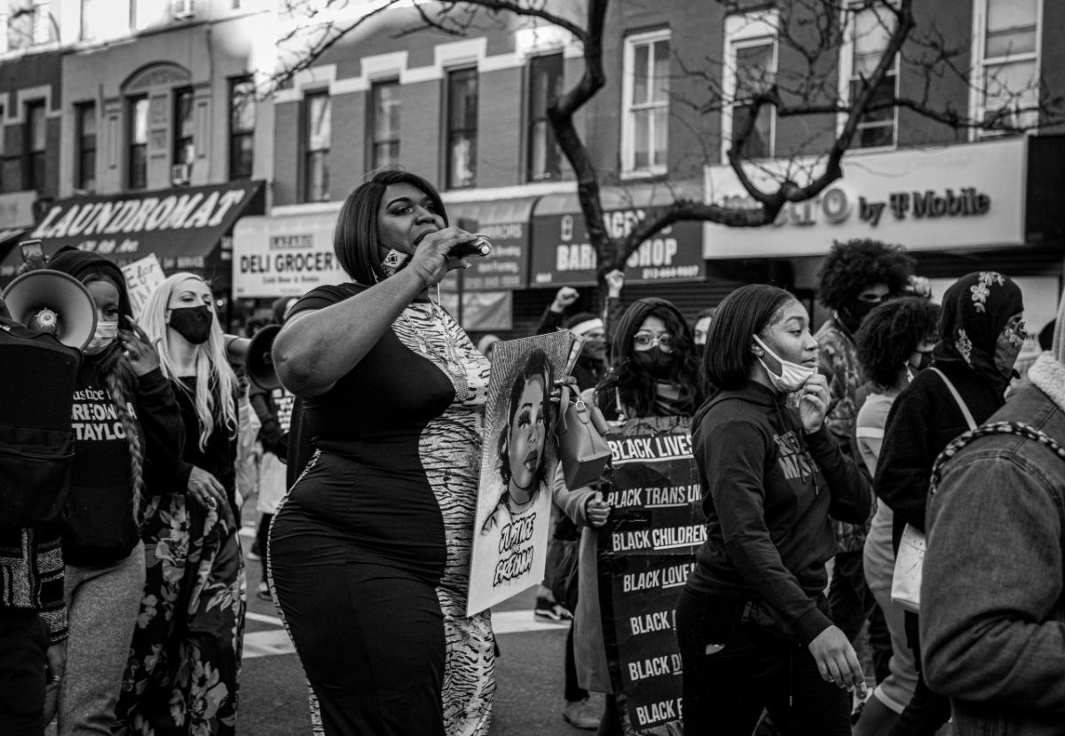 A leader of the protest is standing in the middle of the crowd holding a microphone and a sign that says "Justice for Breonna"