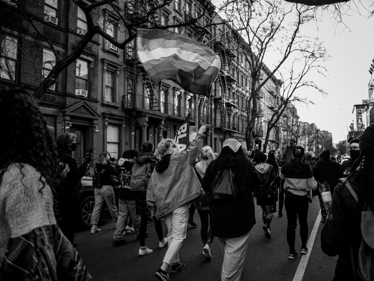 A group of protesters walk on the street, they are photographed from behind. 